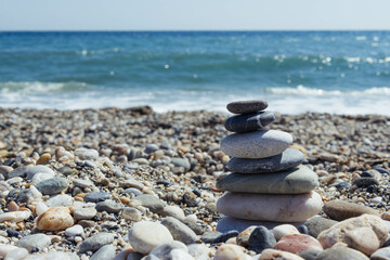 Fototapeta na wymiar Pyramid of sea pebbles on a sunny sandy beach. The concept of life 
