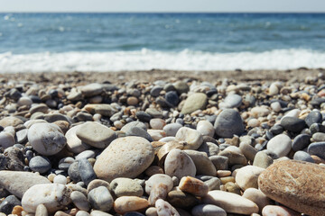 a beach with dark and light pebbles, blue sea, there is a background