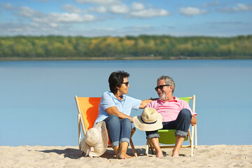 travel concept - smiling happy couple in deck chairs at the beach