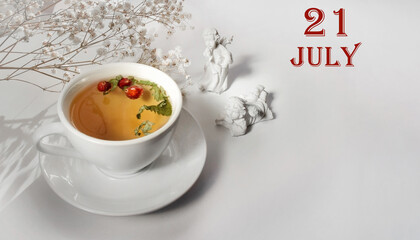 calendar date on light background with a porcelain cup of green tea, white gypsophila and angels with copy space. July 21 is the twenty first day of the month