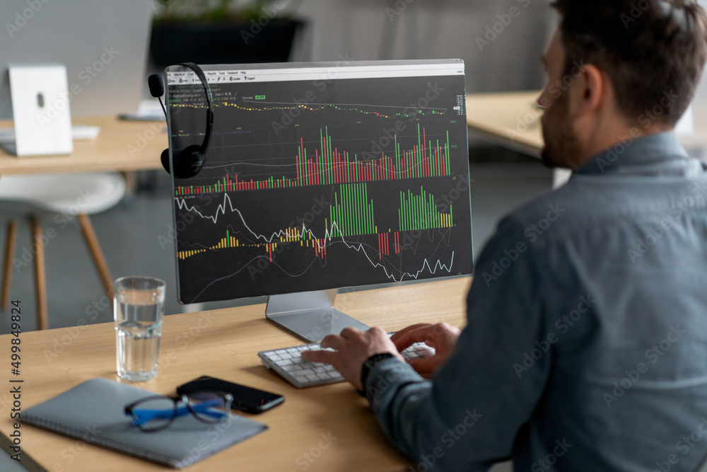 Poster Unrecognizable mature businessman sitting at workdesk in office and typing on keyboard with graph on computer monitor