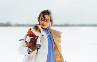 Portrait of an attractive woman with a Jack Russell dog in her arms while walking on a snowy street...