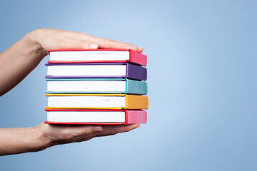 Female hands holding pile of books over light blue background. Education, self-learning, book swap,...