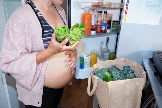 Pregnant woman putting away healthy groceries in kitchen