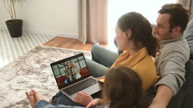 Family of four using laptop for video connection with grandparents or family. Multiracial mom, dad and two kids waving in webcam of the laptop, video call, virtual meeting concept