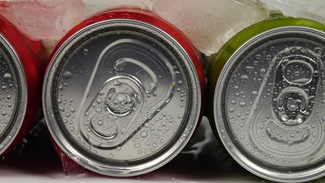 Water droplets from melting ice drip down the aluminum cans with beverages lying in row in the ice