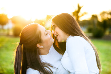 Two happy woman friends laughing face to face in a park with a sunset background. Concept of sisters, family, love, friendship, happiness, couple, sisterhood, jokes and health. 
