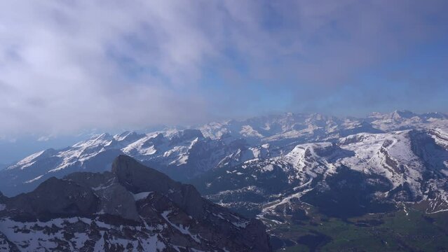 Snow capped mountains with beautiful panoramic view over the Swiss Alps with Toggenburg Valley seen from Säntis peak on a blue cloudy spring morning. Movie shot April 19th, 2022, Säntis, Switzerland.