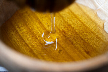 Golden honey flows from the stick into a wooden jar. Aromatic nectar dripping from honey-dipper....