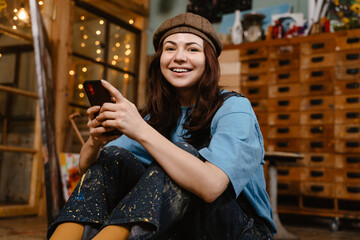 Young woman artist using mobile phone while sitting on floor