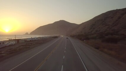 Motorcyclist riding fast at sunset on Pacific coast highway during sunset, Aerial