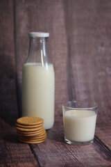 Vaso de leche con galletas con una botella de leche al fondo