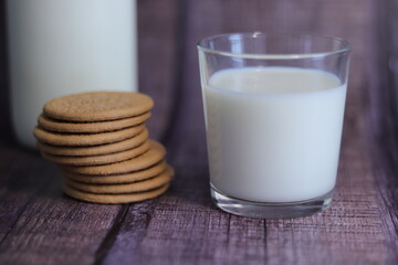 Vaso de leche con galletas y una botella de leche al fondo.