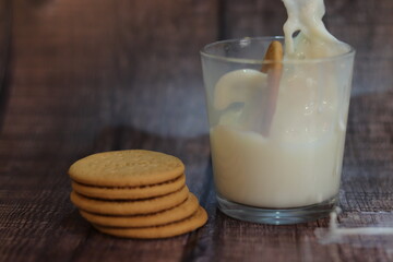Vaso de leche con galleta cayendo dentro y galletas al lado
