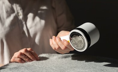 Woman removing lint from fabric with shaver. Handheld electric defuzzer. Clothes care. High quality...