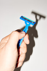 Man's hand with blue razor over gray background