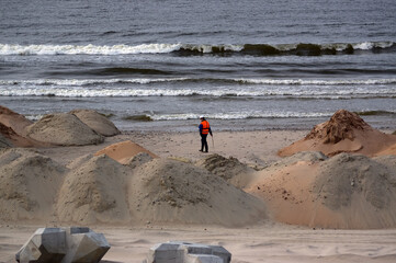 Fototapeta Robotnik pracownik budowlaniec w kasku i kamizelce ochronnej wśród wałów z piasku na plaży. obraz