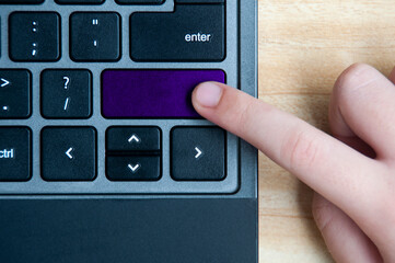 Top view of hand pressing blank purple button on laptop keyboard.