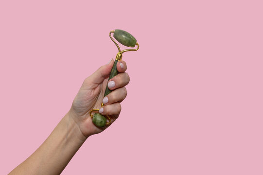 A Woman's Hand Holds A Green Jade Roller For Facial Massage.