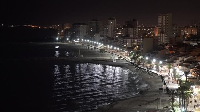 Night time El Campello Costa Blanca coast town Spain with sparkling lights, palm trees, sea and distant people at night time