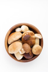 Bunch of fresh forest porcini mushrooms in a round wooden bowl on a white background close up, soft focus, top view, copy space	