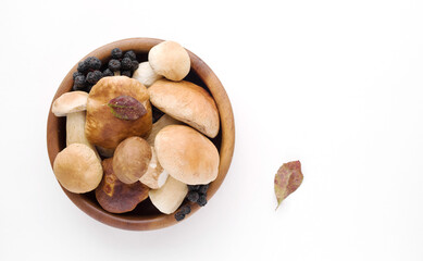 Bunch of fresh forest porcini mushrooms in a round wooden bowl on a white background close up, soft focus, top view, copy space	