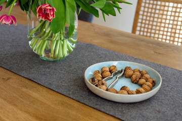 bowl with walnuts and vase with tulips on wooden table indoors