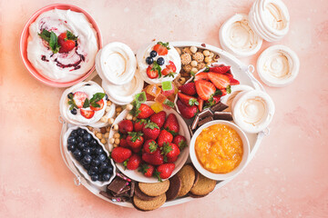 Mini meringue berry sweet dessert platter. Small nests of meringue  on wooden tray with fresh fruits, ginger cookies, toppings, chocolate and whipped cream. Top view, blank space