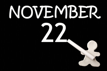 A small white plasticine man writing the date 22 November on a black board. Business concept. Education concept.