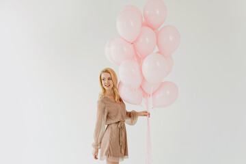 Beautiful blonde woman holding pink balloons on white background.