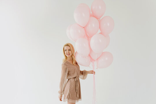 Beautiful blonde woman holding pink balloons on white background.