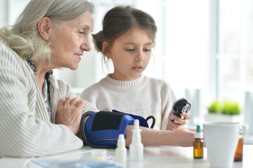 Obraz premium Cute girl and senior woman measuring blood pressure