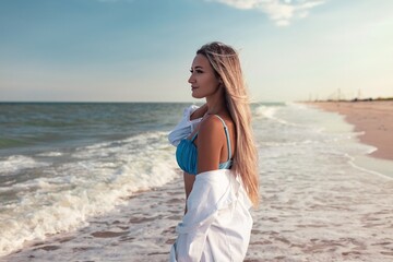 Fototapeta na wymiar Portrait of a girl in a blue swimsuit and white shirt against the background of the blue sea and clear sky