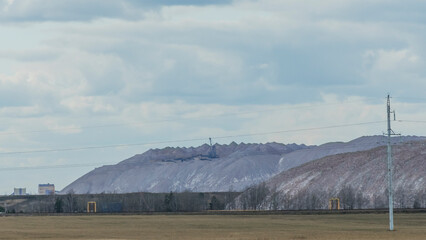 Mountains of empty ore when mining potassium on cloudy sky background. Transportation of an empty rock to a dump.