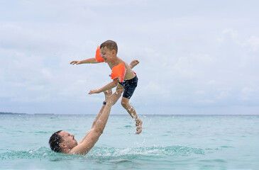 Dad and son are playing in the sea. The father tosses the son up.