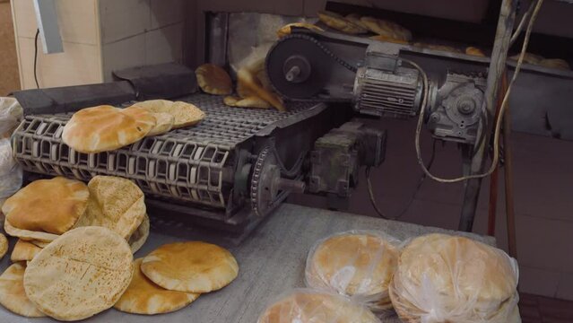 Old machine conveyor system delivering fresh pitta bread baked in local Jordanian bakery, close-up detail