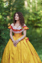 A young woman in an ancient medieval yellow orange dress walks in a green park on a summer day