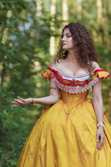 Fototapeta na wymiar A young woman in an ancient medieval yellow orange dress walks in a green park on a summer day