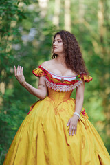 A young woman in an ancient medieval yellow orange dress walks in a green park on a summer day