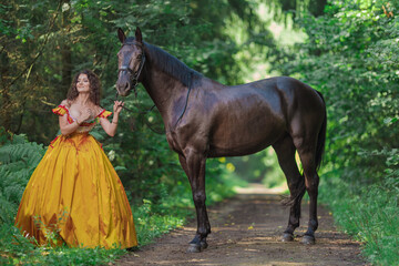 A young woman in a vintage yellow dress walks with a brown horse in a green park on a summer day