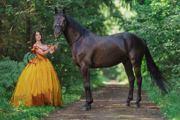 A young woman in a vintage yellow dress walks with a brown horse in a green park on a summer day