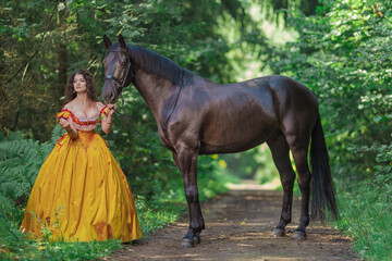A young woman in a vintage yellow dress walks with a brown horse in a green park on a summer day