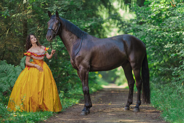 A young woman in a vintage yellow dress walks with a brown horse in a green park on a summer day