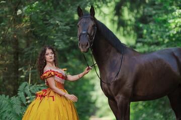A young woman in a vintage yellow dress walks with a brown horse in a green park on a summer day