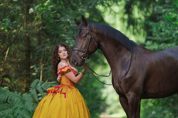 A young woman in a vintage yellow dress walks with a brown horse in a green park on a summer day