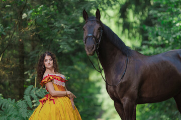 A young woman in a vintage yellow dress walks with a brown horse in a green park on a summer day