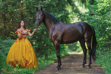 A young woman in a vintage yellow dress walks with a brown horse in a green park on a summer day