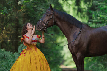 A young woman in a vintage yellow dress walks with a brown horse in a green park on a summer day
