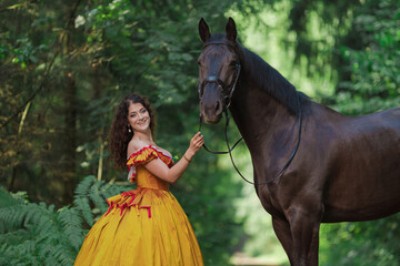 A young woman in a vintage yellow dress walks with a brown horse in a green park on a summer day