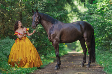 A young woman in a vintage yellow dress walks with a brown horse in a green park on a summer day